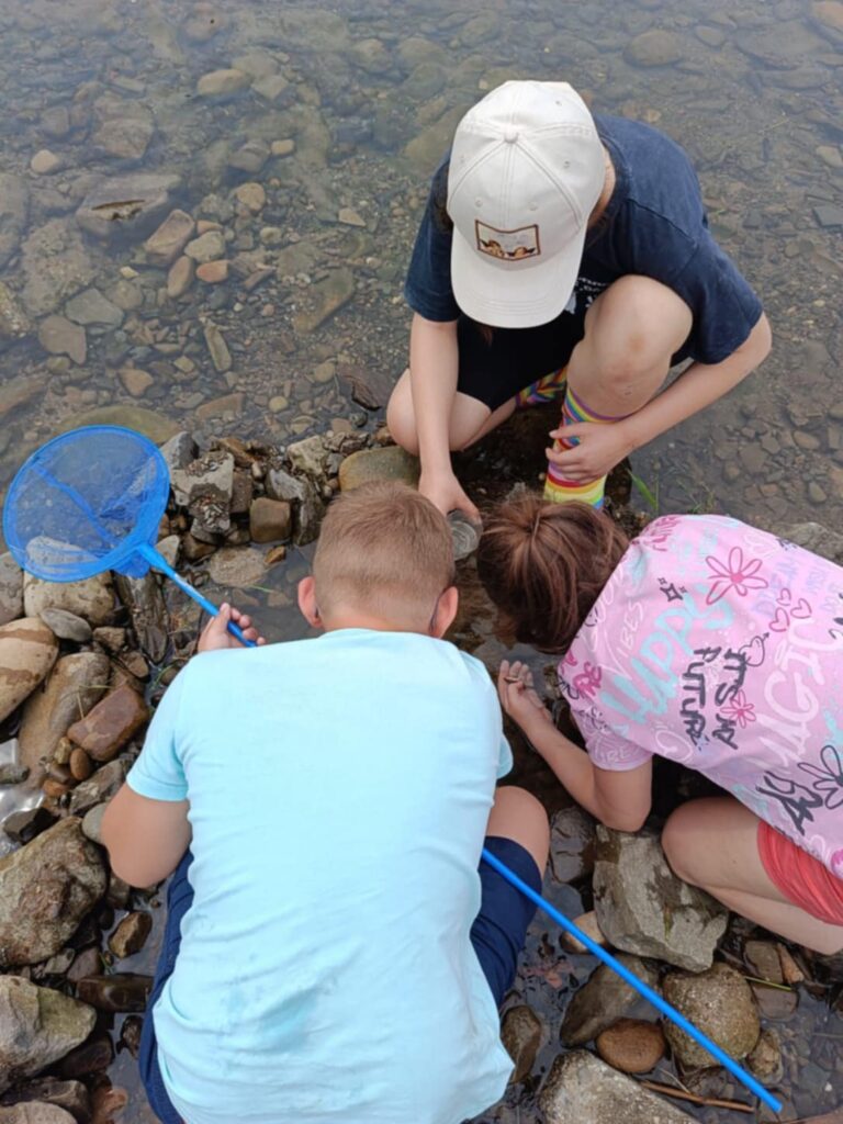 Troje dzieci kuca w rzece, wspólnie coś oglądają